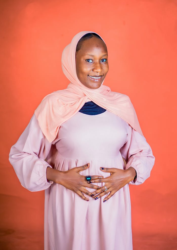 Pregnant woman in pastel clothing with orange background, smiling confidently.